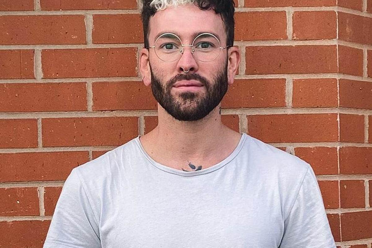 Adam standing against a brick wall with glasses and white T-shirt