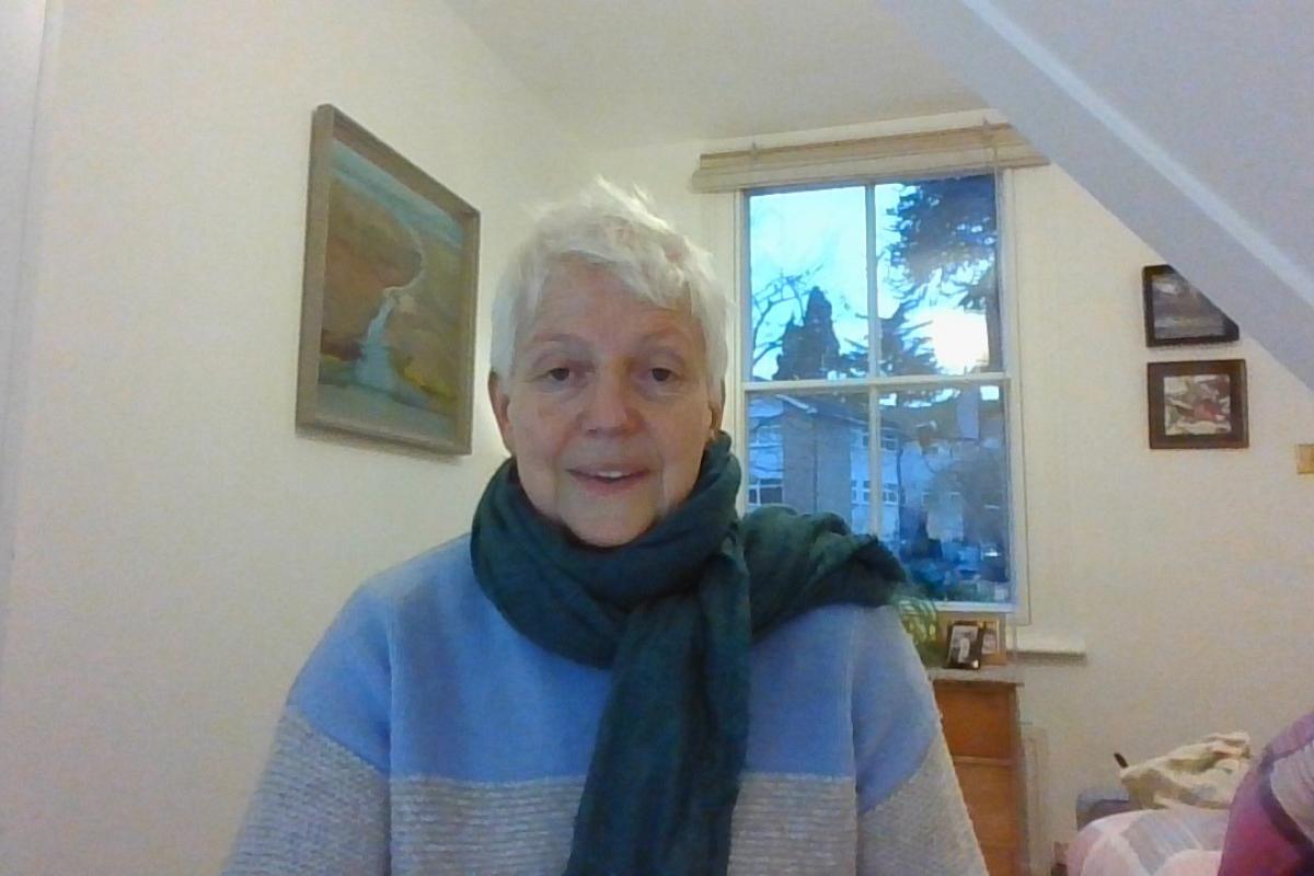 Sue smiling with a scarf and blue and white jumper in a bedroom
