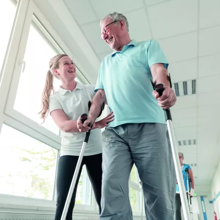 An older man being supported to walk by an OT
